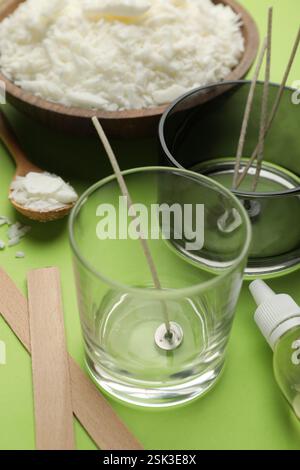 Preparare candele fatte in casa. Cera di soia nel recipiente, vasetti con stabilizzatori, stoppini e olio essenziale su sfondo verde, primo piano Foto Stock