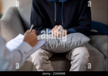 Primo piano di un uomo stressato seduto su un divano, stringendo le mani insieme in frustrazione durante un controllo di salute mentale con uno psicologo. mentale Foto Stock
