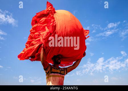 Un lavoratore porta un panno colorato sulla testa mentre si dirige verso la fabbrica dopo che si è asciugato. Narsingdi, Bangladesh. Foto Stock