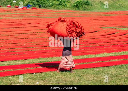 Un lavoratore porta un panno colorato sulla testa mentre si dirige verso la fabbrica dopo che si è asciugato. Narsingdi, Bangladesh. Foto Stock