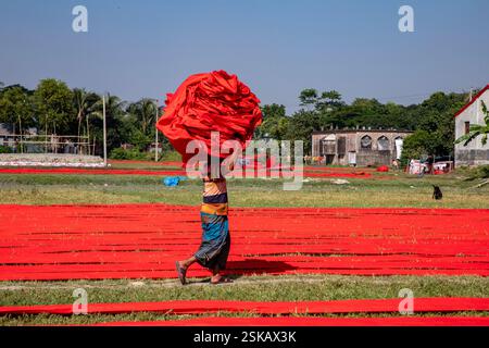 Un lavoratore porta un panno colorato sulla testa mentre si dirige verso la fabbrica dopo che si è asciugato. Narsingdi, Bangladesh. Foto Stock