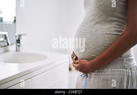 Donna, mani e gravidanza con stomaco per mattina, assistenza sanitaria o igiene in bagno a casa. Primo piano, donna o mamma con la pancia del bambino Foto Stock