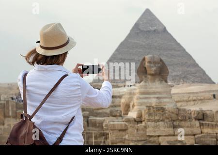 Giovane donna in piedi che scatta una foto di fronte alla grande Sfinge di Giza con le incredibili piramidi sullo sfondo. La Valle dei Re, il Cairo, Egg Foto Stock