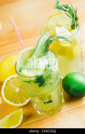 Cocktail al limone e alle erbe preparati al momento serviti con decorazioni agli agrumi su un tavolo di legno in un ambiente luminoso Foto Stock
