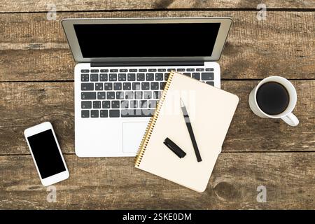 Spazio di lavoro con un computer portatile, un notebook, una penna, uno smartphone e un caffè su un tavolo in legno rustico Foto Stock