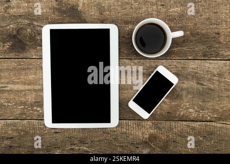 Dispositivi digitali e una tazza di caffè su un tavolo in legno rustico in un ambiente tranquillo Foto Stock