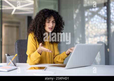 Donna insoddisfatta e turbata che lavora con un notebook all'interno dell'ufficio sul posto di lavoro, donna d'affari che legge un messaggio online, e-mail con cattive notizie, delusa e triste. Foto Stock