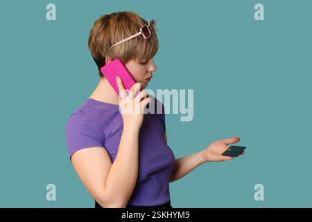 Una ragazza incredulo e moderna fa pubblicità, fa acquisti online, tiene in mano una carta di credito e parla su uno smartphone. Foto Stock