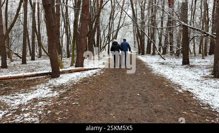 Coppia matura che va su un sentiero innevato nella pineta invernale. Marito anziano e moglie camminano attraverso il sentiero nel bosco di conifere. Coppia più vecchia di Foto Stock