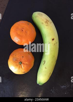 Due mandarini formano gli occhi, bocca di banana. Allegro arrangiamento gastronomico, Braga, Portogallo. Giallo, arancio, sfondo scuro. Foto Stock