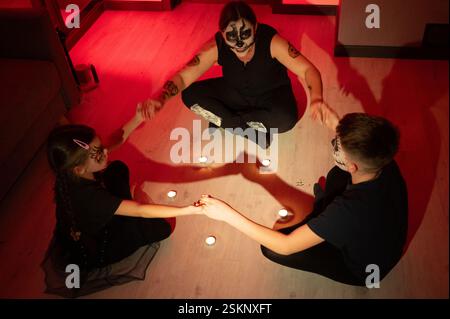 Una famiglia si impegna in una tradizione di Halloween. Un adulto con il viso del cranio si siede con due bambini, tutti tenendo le mani intorno a piccole candele in un lieve li Foto Stock