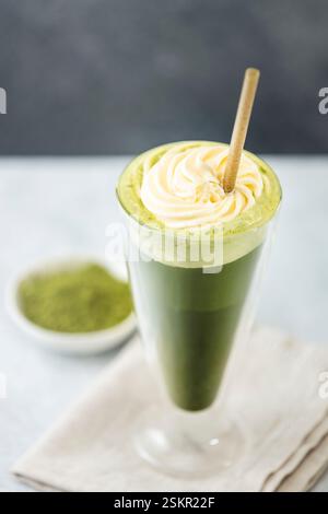 Rinfrescante latte matcha ghiacciato con panna montata e servito con una cannuccia eco-compatibile, promuovendo uno stile di vita sano e sostenibile Foto Stock