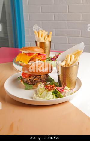 Hamburger gourmet di manzo e pollo fritto serviti con patatine fritte tagliate a mano su un bicchiere di metallo dorato e un pizzico di verdure. Foto Stock