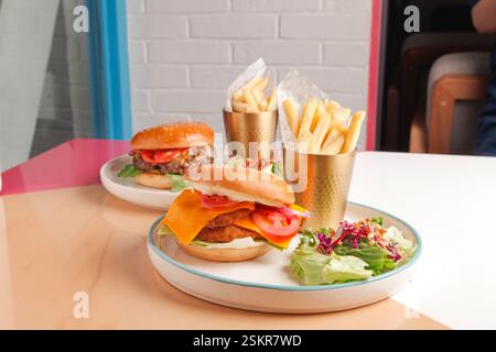 Hamburger gourmet di manzo e pollo fritto serviti con patatine fritte tagliate a mano su un bicchiere di metallo dorato e un pizzico di verdure. Foto Stock