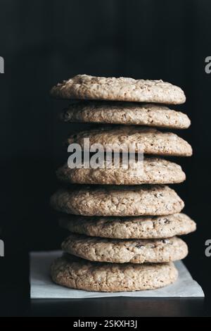 Un'alta pila di biscotti fatti in casa con scaglie di cioccolato senza glutine, con una consistenza rustica, posti su carta pergamena su sfondo scuro Foto Stock