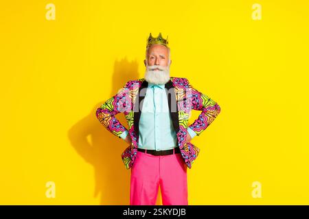 Ritratto fotografico di un attraente pensionato, un re orgoglioso e fiducioso, vestito con abiti rosa colorati e fantasiosi, isolato su sfondo giallo Foto Stock