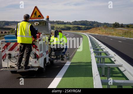 Produzione di una linea di vernice bianca di sicurezza, utilizzando una macchina speciale, su un'autostrada in costruzione. Foto Stock
