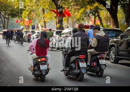 Un gruppo di giovani amici vietnamiti su tre scooter motociclistici e senza casco naviga lungo una strada vicino al lago Hoan Kien nel centro di Hanoi, Viet Foto Stock