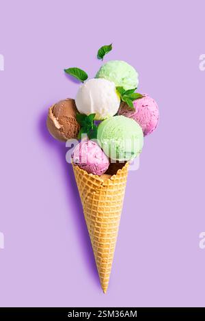 Il gelato si prepara in un cono croccante per waffle su sfondo viola pastello, con un'ampia scelta di piatti. Tanti gelati biologici colorati con foglie di menta, Foto Stock