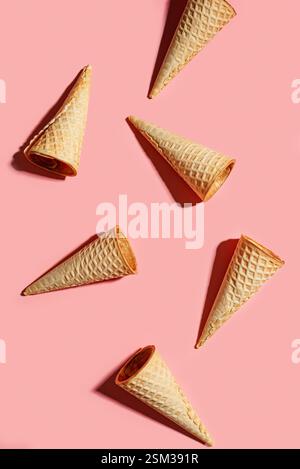 Disposizione creativa dei coni per cialde di gelato su sfondo rosa pastello, vista dall'alto. Concetto di dessert dolce estivo. Foto Stock