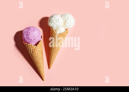 Due coni di gelato croccanti al gusto di vaniglia e mirtillo su sfondo rosa pastello, vista dall'alto, spazio copia. Creativi gelati alla moda, estate des Foto Stock