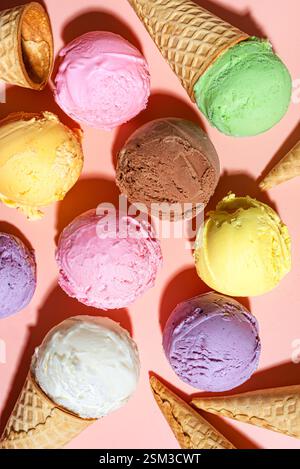 Vari cucchiai per gelato su sfondo rosa, design creativo con luce dura. Molti bicchieri per gelato colorato biologico e coni per cialde come sfondo. Foto Stock