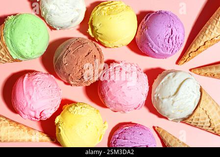 Cucchiai per gelato assortiti su sfondo rosa pastello, vista dall'alto. Molti gelati italiani biologici e coni per cialde, dessert estivi. Foto Stock
