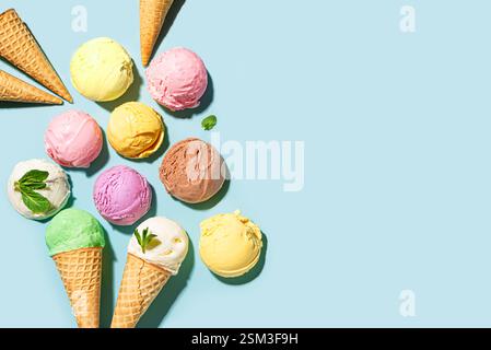 Palline di gelato assortite su sfondo blu, vista dall'alto, spazio per copiare. Vari gelati o gelato con coni di waffle, dessert estivo salutare creativo Foto Stock