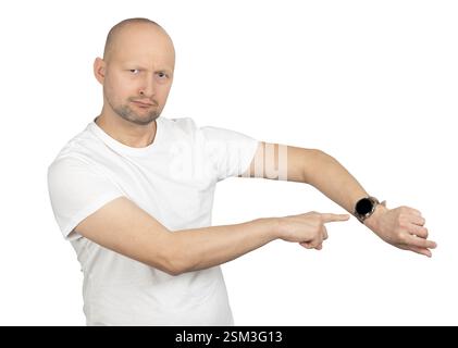 Un uomo caucasico calvo con stoppie leggere indossa una t-shirt bianca e punta il suo orologio da polso. Foto Stock