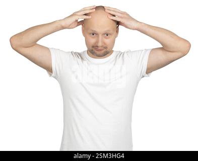 Un uomo caucasico calvo con la barba corta indossa una t-shirt bianca e mette entrambe le mani sulla testa con un'espressione sorpresa. Foto Stock
