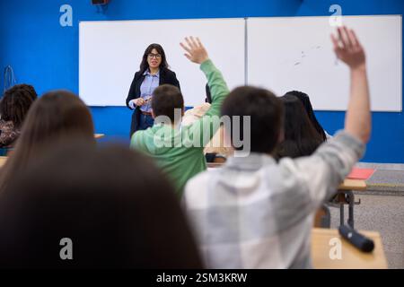 Studenti che alzano le mani in classe durante la lezione con l'insegnante Foto Stock