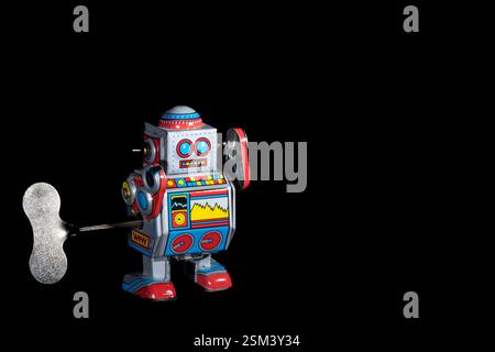 Robot giocattolo classico in stile retrò con colori vivaci e meccanismo a vento, posizionato su uno sfondo nero liscio, che ne mette in risalto il design e nosta Foto Stock