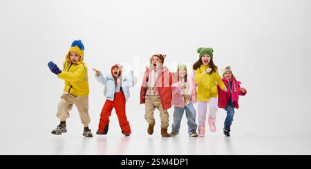 Gruppo di bambini, ragazze e ragazzi, vestiti caldi invernali che corrono, alzando le mani di felicità e divertimento sullo sfondo bianco dello studio Foto Stock