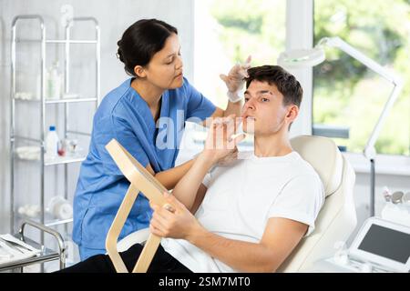 Giovane cosmetologa che esamina il volto di un giovane uomo Foto Stock