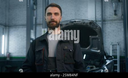Ritratto di un dipendente tecnico meccanico di auto sorridente in uniforme da lavoro che guarda fotocamera alla stazione di servizio di riparazione auto felice maschio specialista caucasico Foto Stock