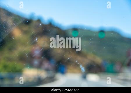 Vista astratta attraverso il parabrezza di un'auto con polvere, graffi, paesaggio sfocato e semafori verdi sullo sfondo Foto Stock