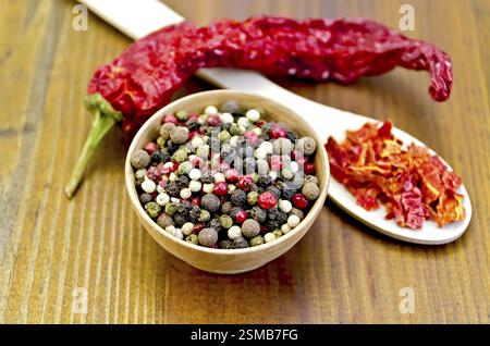 Pepe piselli in una ciotola di legno, scaglie di peperone rosso in un cucchiaio di legno, un pod di pepe rosso contro un pannello di legno Foto Stock