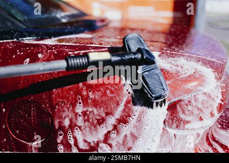 Un'auto rossa che viene pulita con sapone suona utilizzando una spazzola e uno spray per ugelli Foto Stock