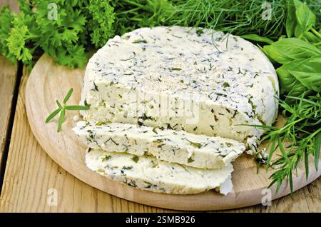 In casa formaggio rotondo con erbe e spezie tagliato a fettine su una tavola di legno Foto Stock