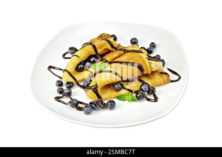 Due frittelle con mirtilli, menta, glassa di cioccolato su una piastra bianca isolata su sfondo bianco Foto Stock