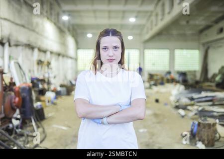 La donna sta in piedi con le braccia incrociate in un'officina disordinata Foto Stock