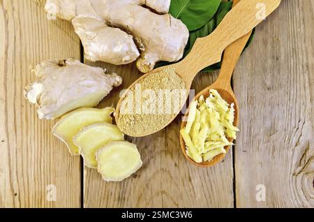 Grattugiato e lo zenzero in polvere in due cucchiai di legno, radice di zenzero, foglie verdi sul pannello di legno Foto Stock