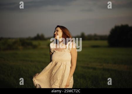 Una donna che indossa un abito sorride brillantemente in un campo al tramonto, trasudando un'atmosfera allegra e naturale Foto Stock