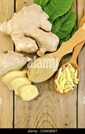 Grattugiato e lo zenzero in polvere in due cucchiai di legno, radice di zenzero, foglie verdi sullo sfondo del pannello di legno Foto Stock