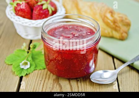 Confettura di fragole in un barattolo di vetro a strati, bun, fragole in un cestello, igienico, cucchiaio su una tavola di legno Foto Stock