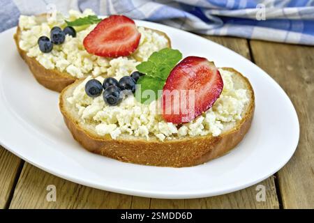 Fette di pane con crema di ricotta, menta, mirtilli e fragole su una piastra su un tavole di legno sfondo Foto Stock