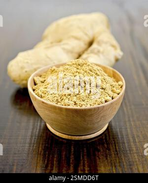 Ciotola di legno con lo zenzero in polvere, radice di zenzero sullo sfondo del pannello di legno Foto Stock