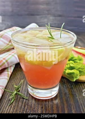La limonata con il rabarbaro e il rosmarino in un vetro, gli steli e foglie di rabarbaro, un centrino su tavole di legno sfondo Foto Stock
