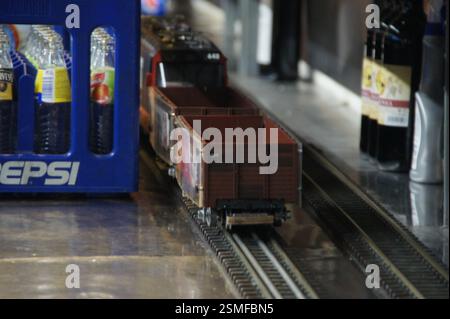 Modellare il treno sui binari accanto al bar. Treno rosso e nero con auto marrone aperta. Repubblica Ceca. Scatola Pepsi e bottiglie di vino sullo sfondo. Repubblica Ceca. Foto Stock