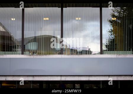 Un cartello grigio vuoto è montato all'esterno di un elegante complesso di uffici, che riflette l'ambiente urbano e offre spazio per il branding personalizzato in Germania. Foto Stock